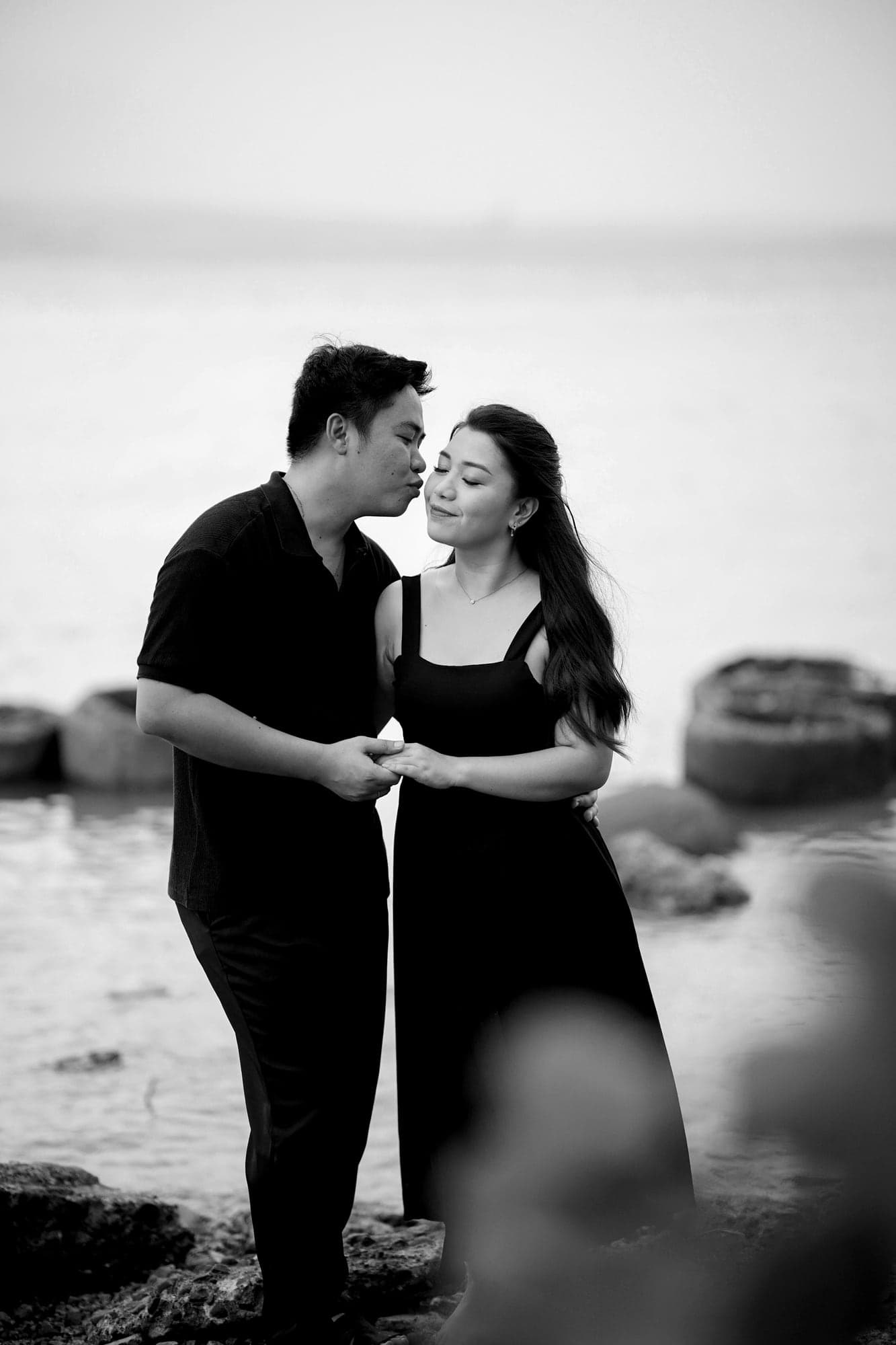 RK kissing Ina's cheek by the sea, both dressed in black